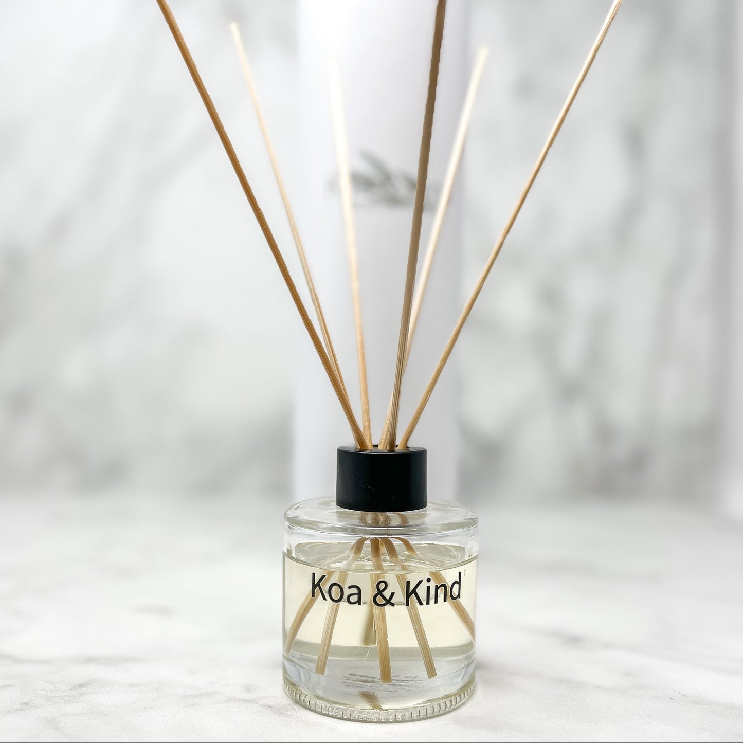 Reed diffuser with wooden sticks in a clear bottle labeled 'Koa & Kind' on a light background