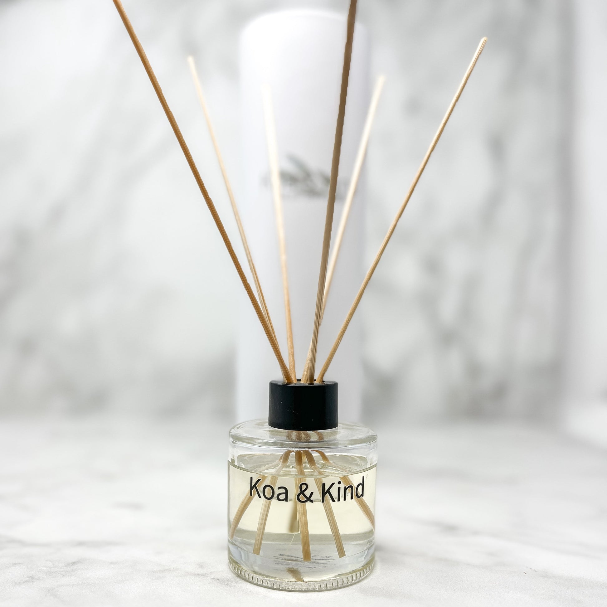 Reed diffuser with wooden sticks in a clear bottle labeled 'Koa & Kind' on a light background
