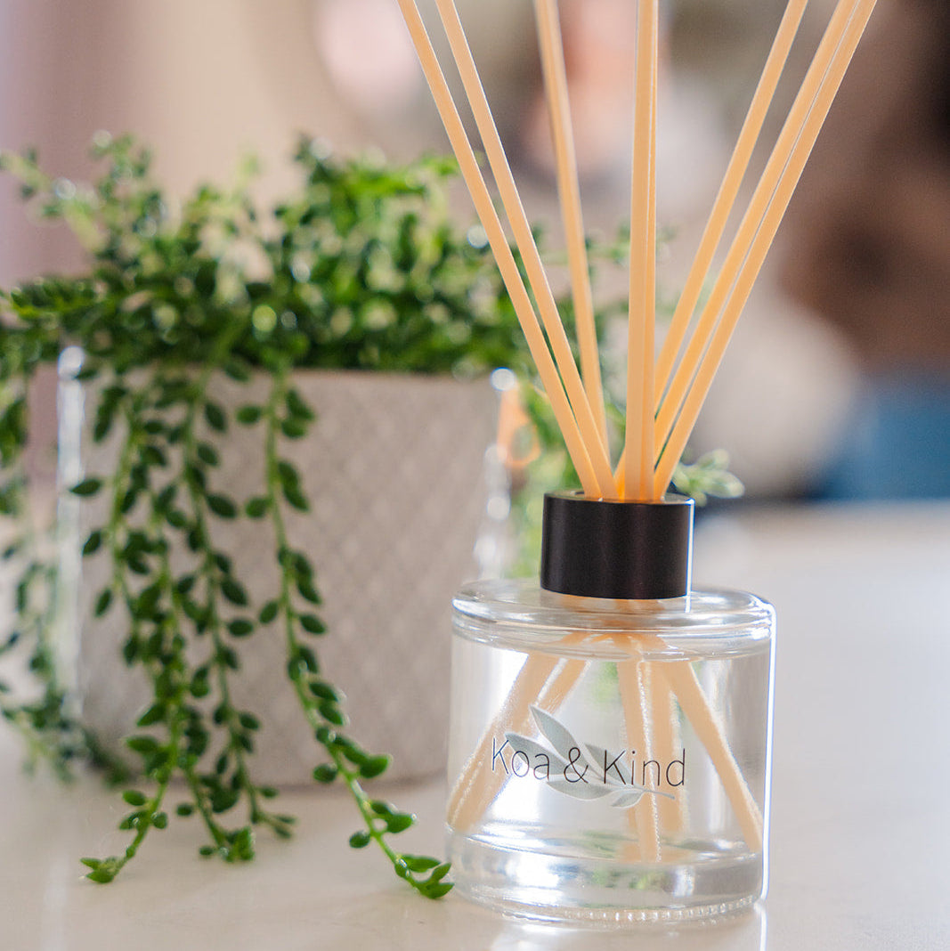 Reed diffuser with wooden sticks in a clear bottle on a surface with greenery in the background