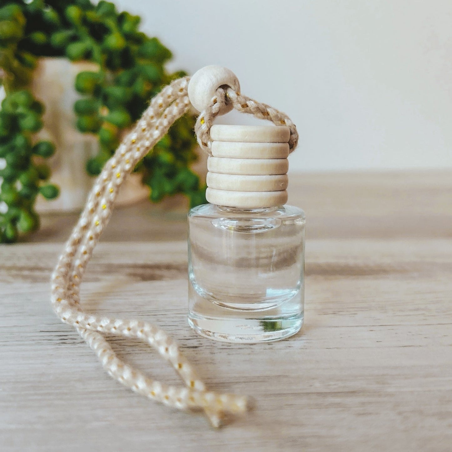 Clear glass bottle with wooden cap and rope on a light wooden surface with greenery in the background